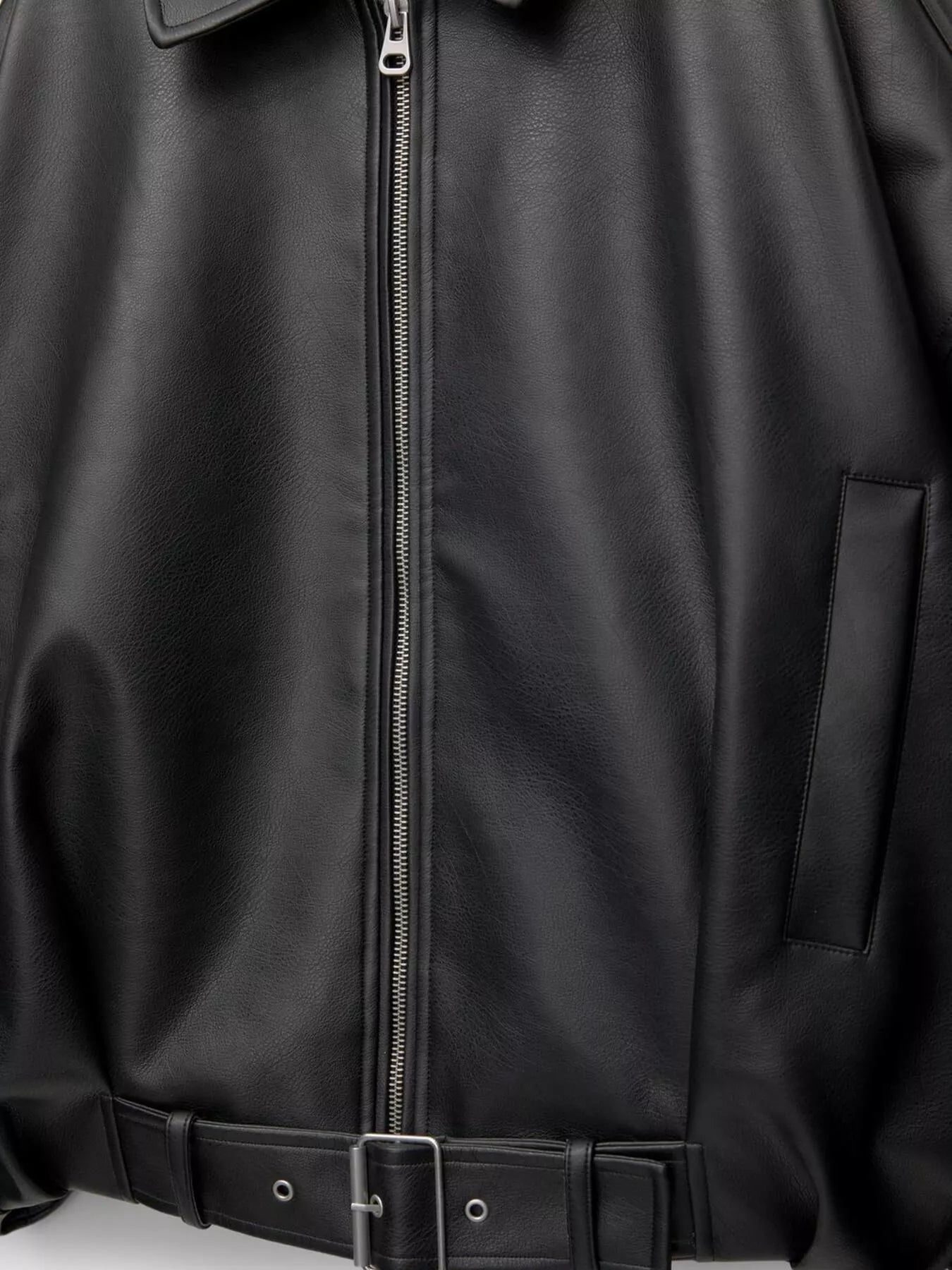Close-up of a black leather jacket with a front zipper, side pocket, and matching black belt with silver buckle.