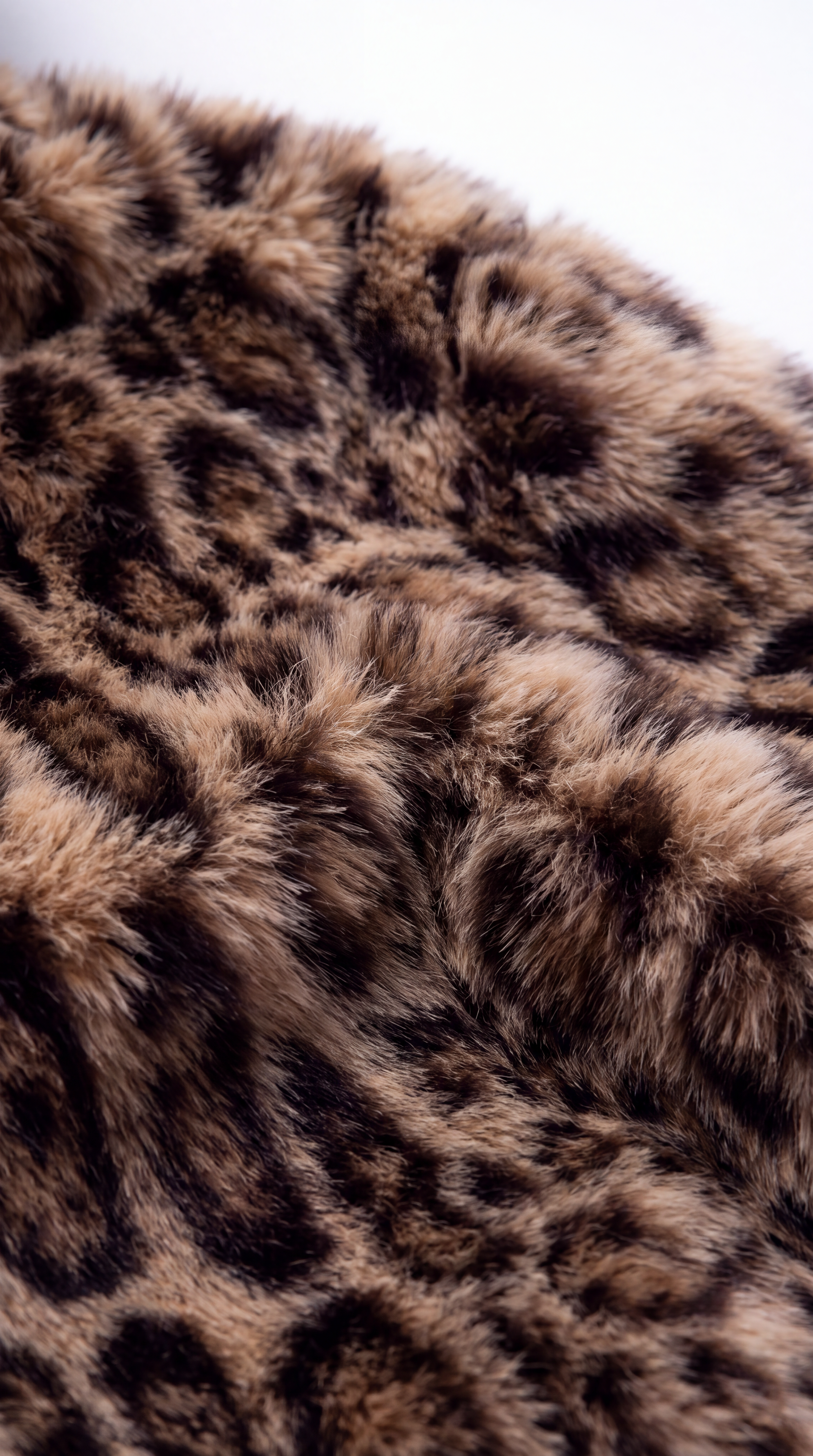 Close-up of a leopard print faux fur fabric with brown, black, and beige tones, shown against a plain white background.