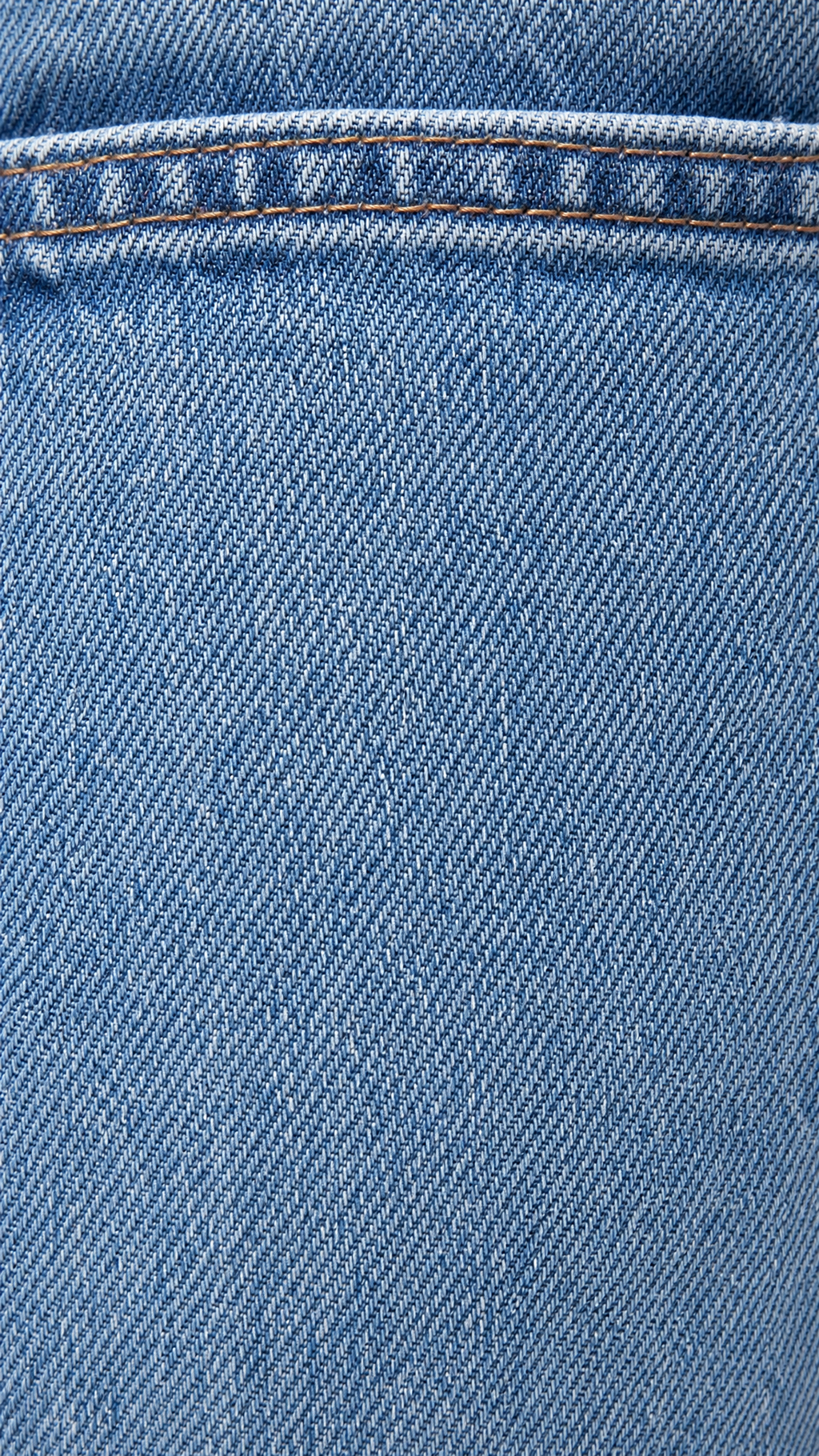 Close-up of light blue denim fabric with diagonal twill weave and a horizontal seam with contrasting brown stitching.