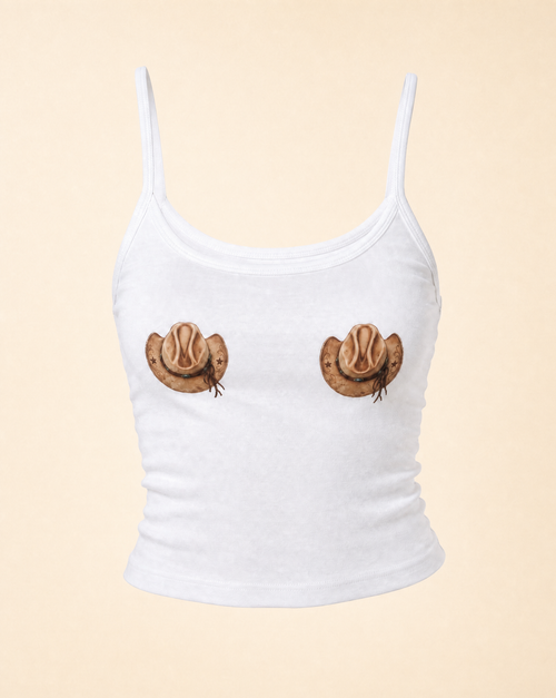 A white ribbed camisole tank top with spaghetti straps, featuring a novelty graphic print of two cowboy hats positioned where the chest should be, set against a solid pale peach background.