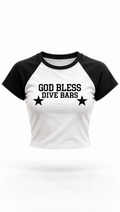 A black and white raglan crop top t-shirt featuring the text 'GOD BLESS DIVE BARS' and two black stars printed on the front, displayed against a plain white background.
