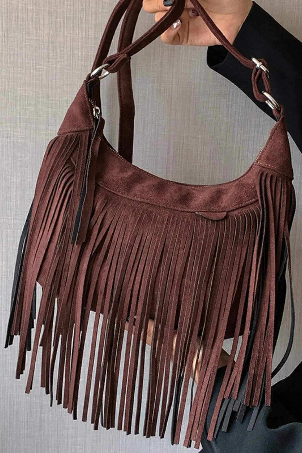 Brown suede handbag with fringe details on a neutral background