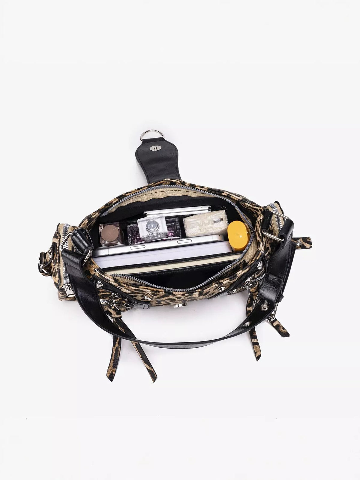 An open fanny pack with a leopard print pattern and black leather trim, shown from a top-down view on a white background. The pack is filled with various items, including a camera, notebooks, and a yellow container.