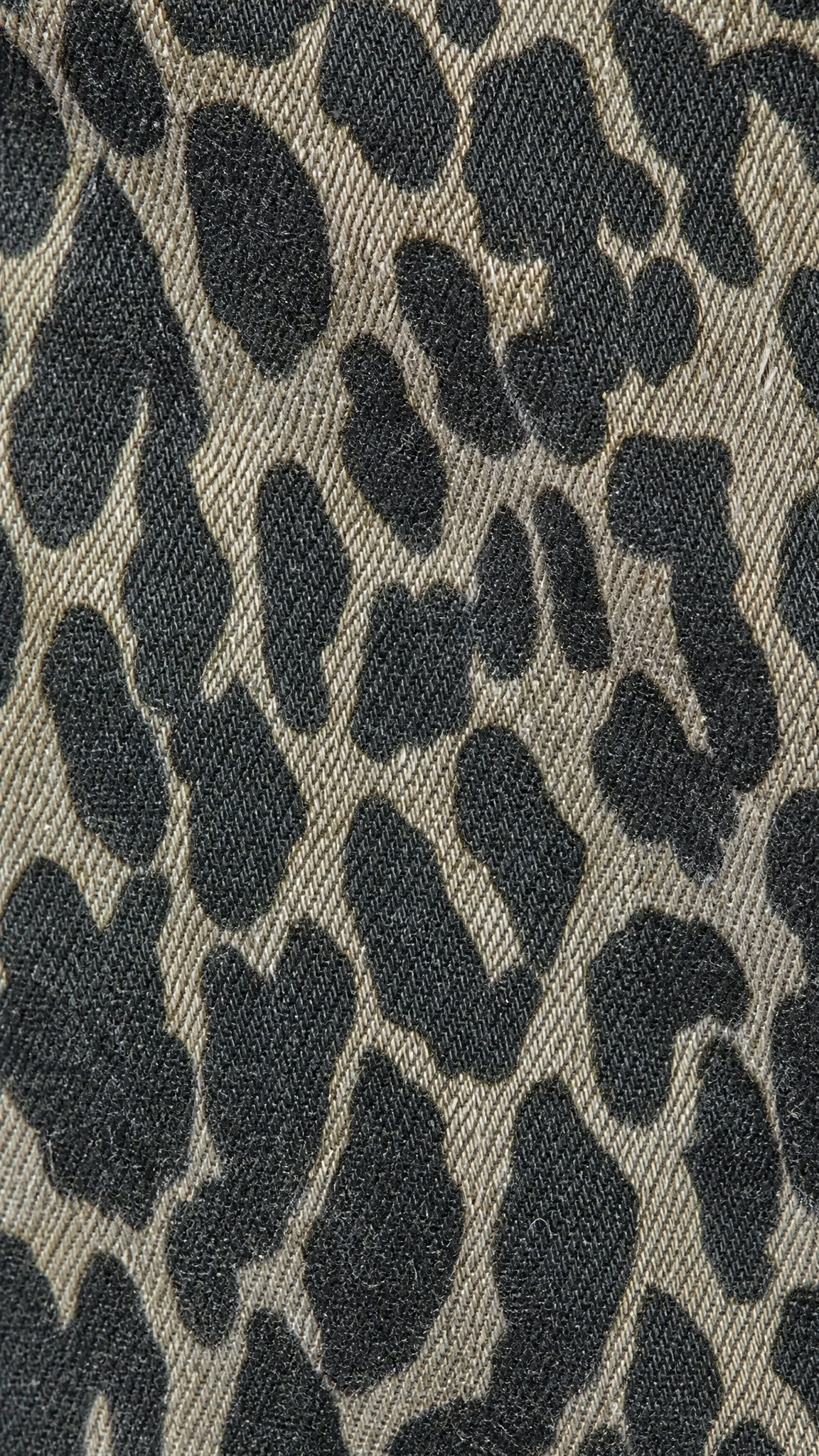 Close-up of a leopard print fabric texture with black irregular spots on a warm taupe-beige woven background.