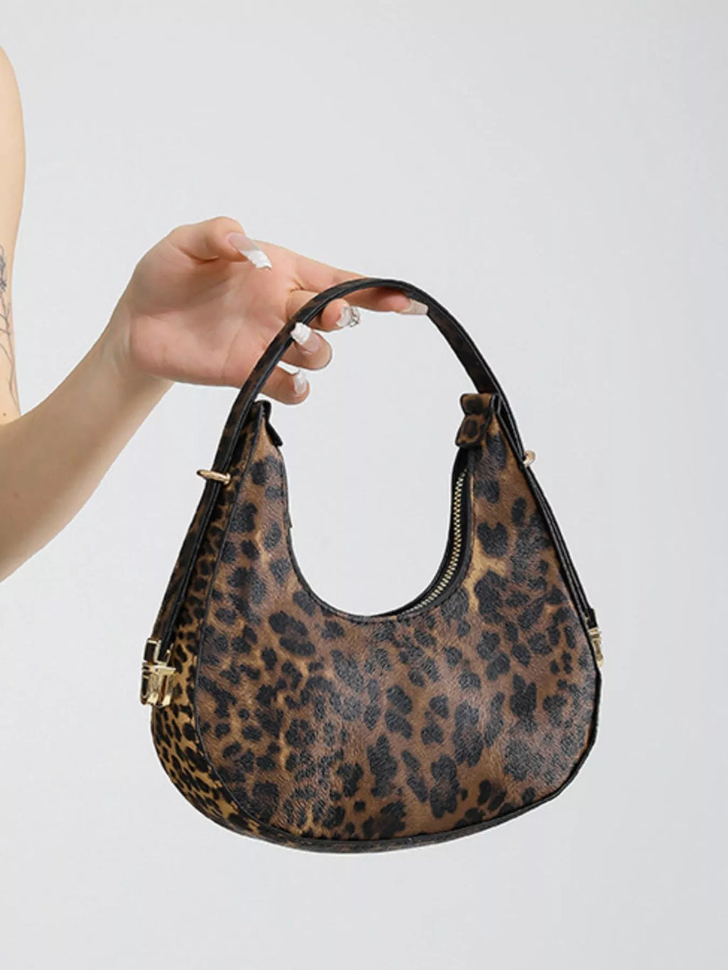 Leopard print handbag held by a person against a light gray background