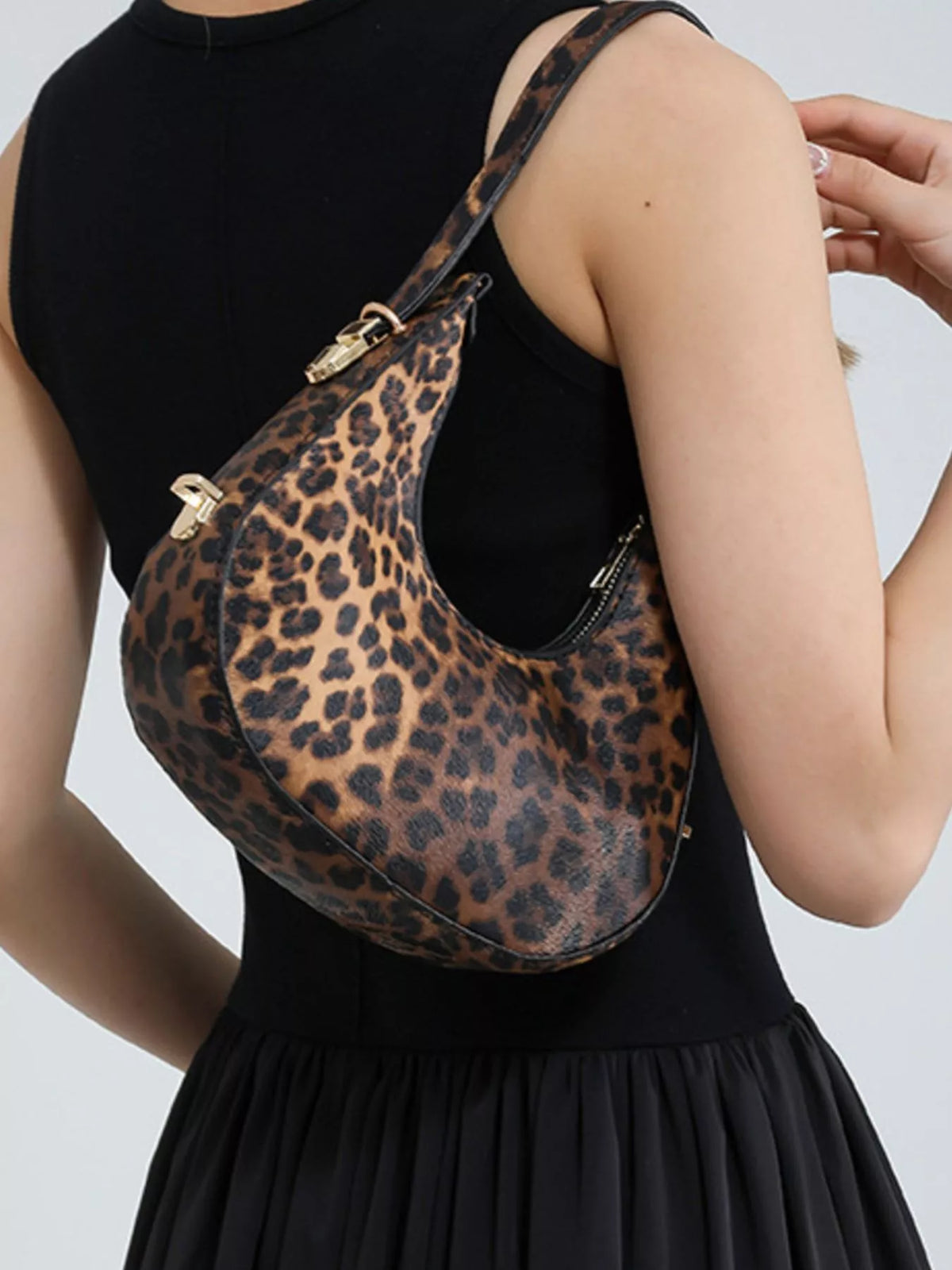 Leopard print handbag held by a person wearing a black dress on a light gray background