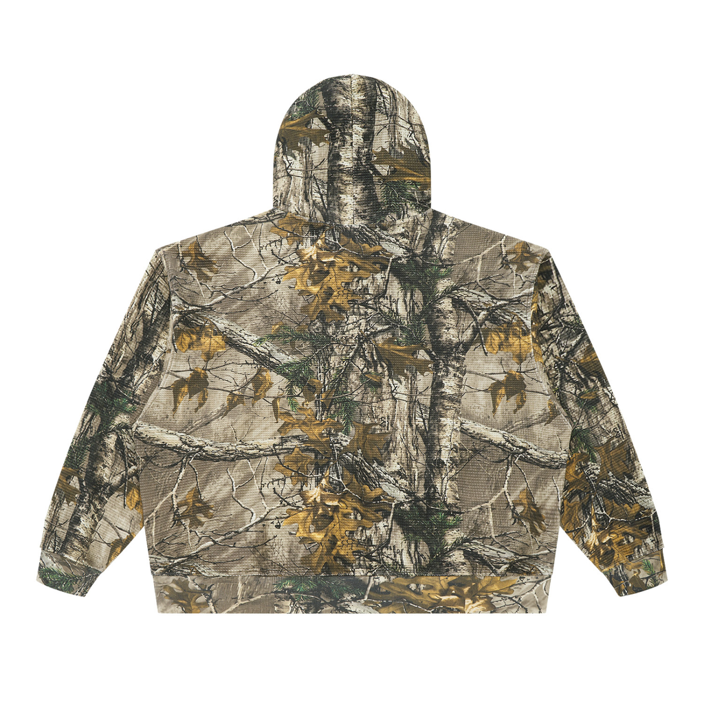 A hooded jacket shown from the back, featuring an all-over woodland camouflage pattern with branches, leaves, and tree bark in beige, brown, green, and gray tones.