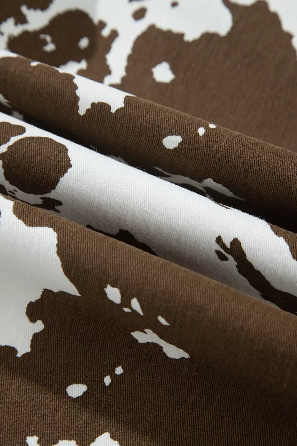 A close-up of draped fabric with a brown and white cow print pattern, showing the texture and folds of the material.