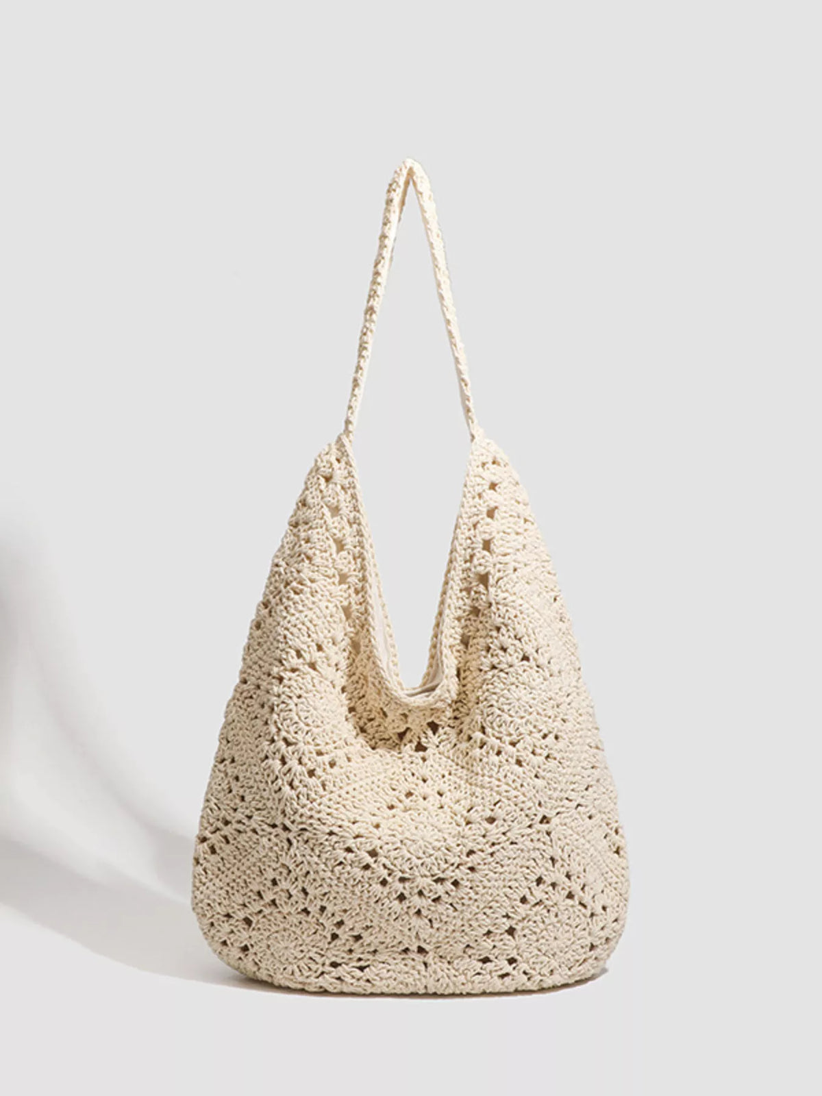 A cream-colored crochet slouchy shoulder bag with an openwork pattern and a single shoulder strap, photographed on a light gray background.