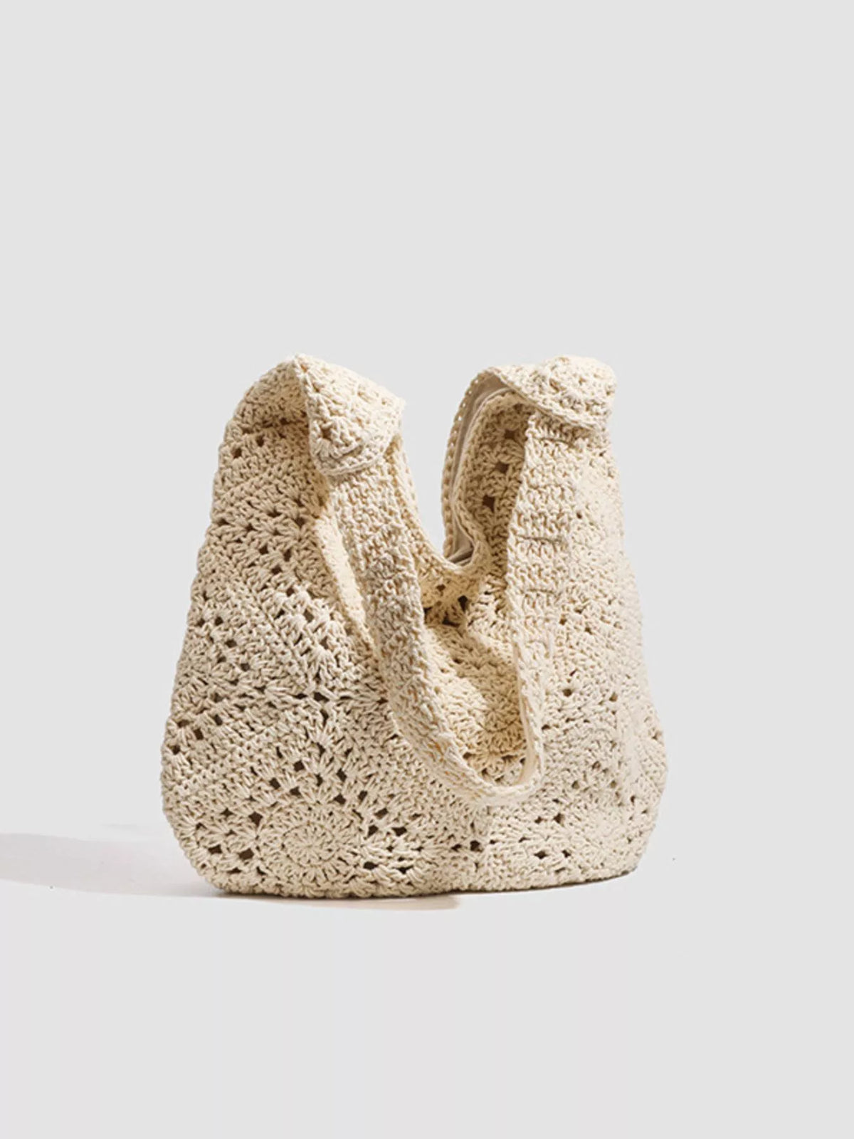 A chunky, open-knit crochet shoulder bag in a natural cream color, photographed against a solid light gray background.